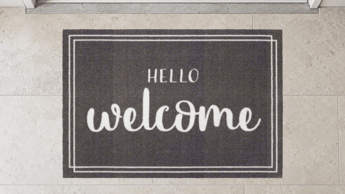 Graue Fußmatte mit weißem „HELLO welcome“-Motiv auf Steinboden